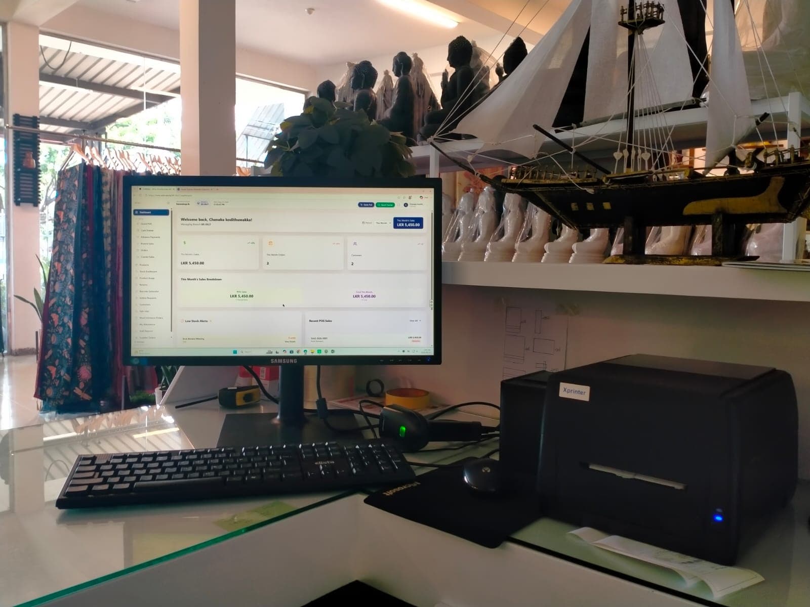 SellMate sales dashboard beside an Xprinter receipt printer and barcode scanner at Sareeshop.lk